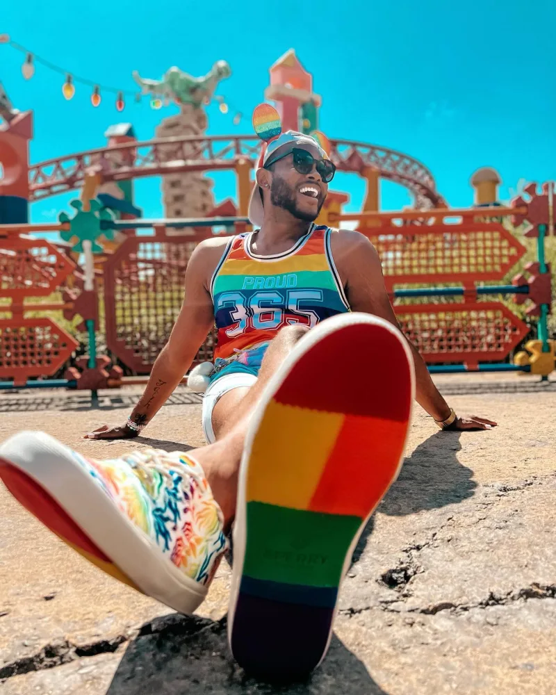 Creator in rainbow mouse ears poses at disneyland wearing Sperry PFLAG rainbow bottom shoes