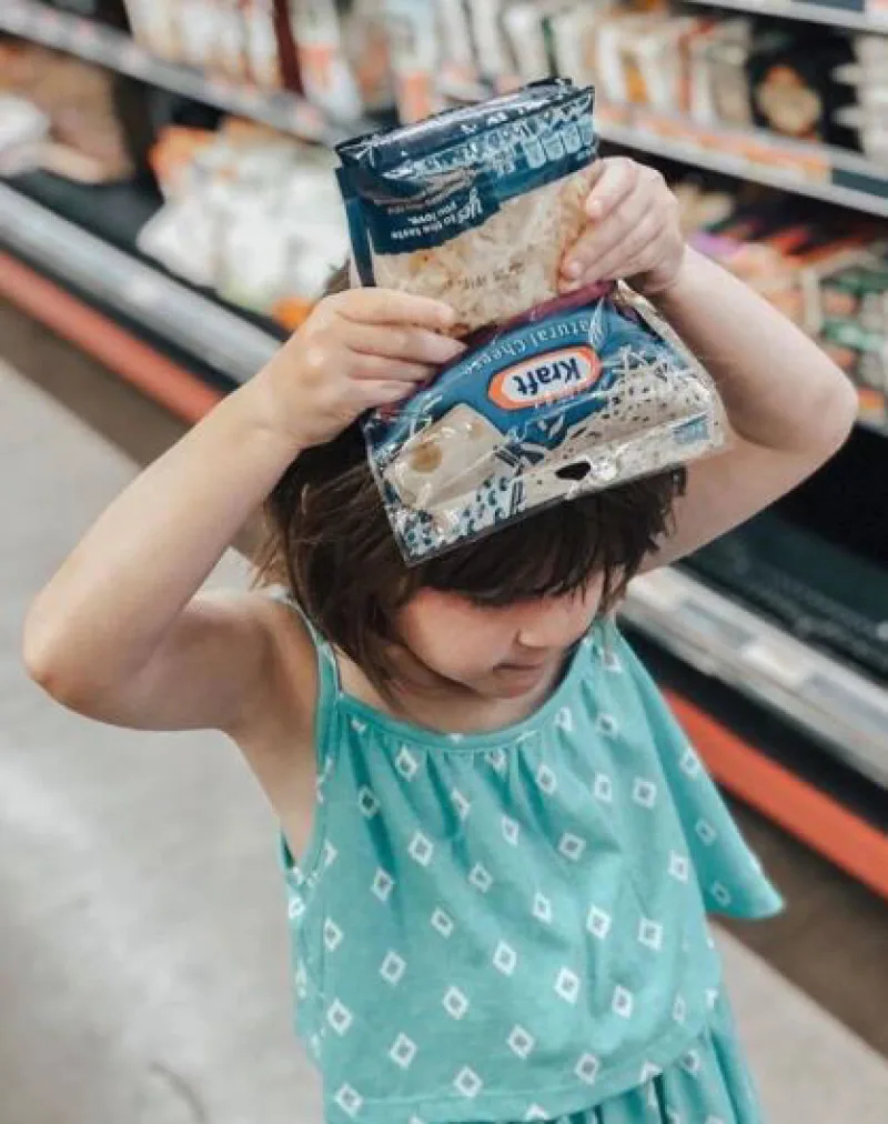 Girl holding bag of Kraft cheese over her head in a grocery store