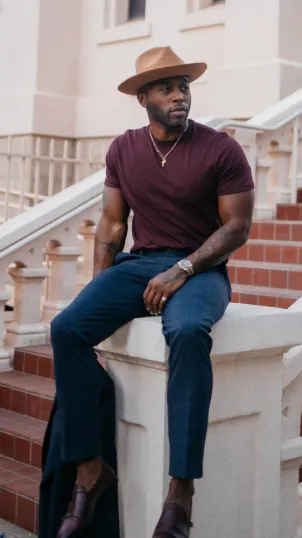 Influencer poses while sitting on a front porch with a brown hat on