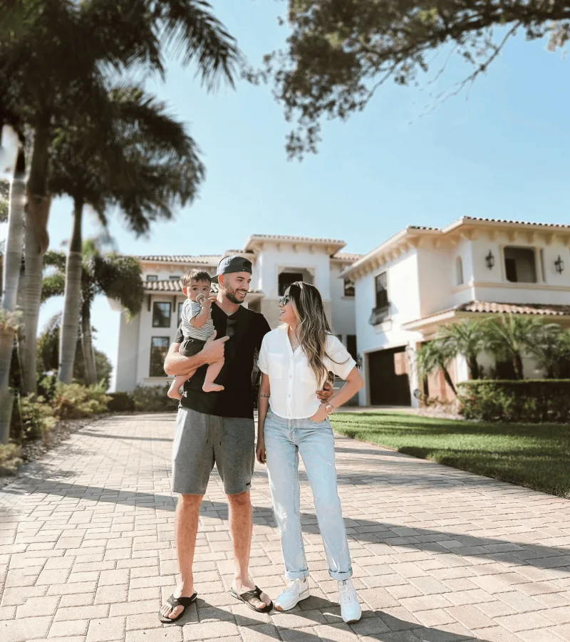 Creator with her partner and child stand proudly outside of a large white home