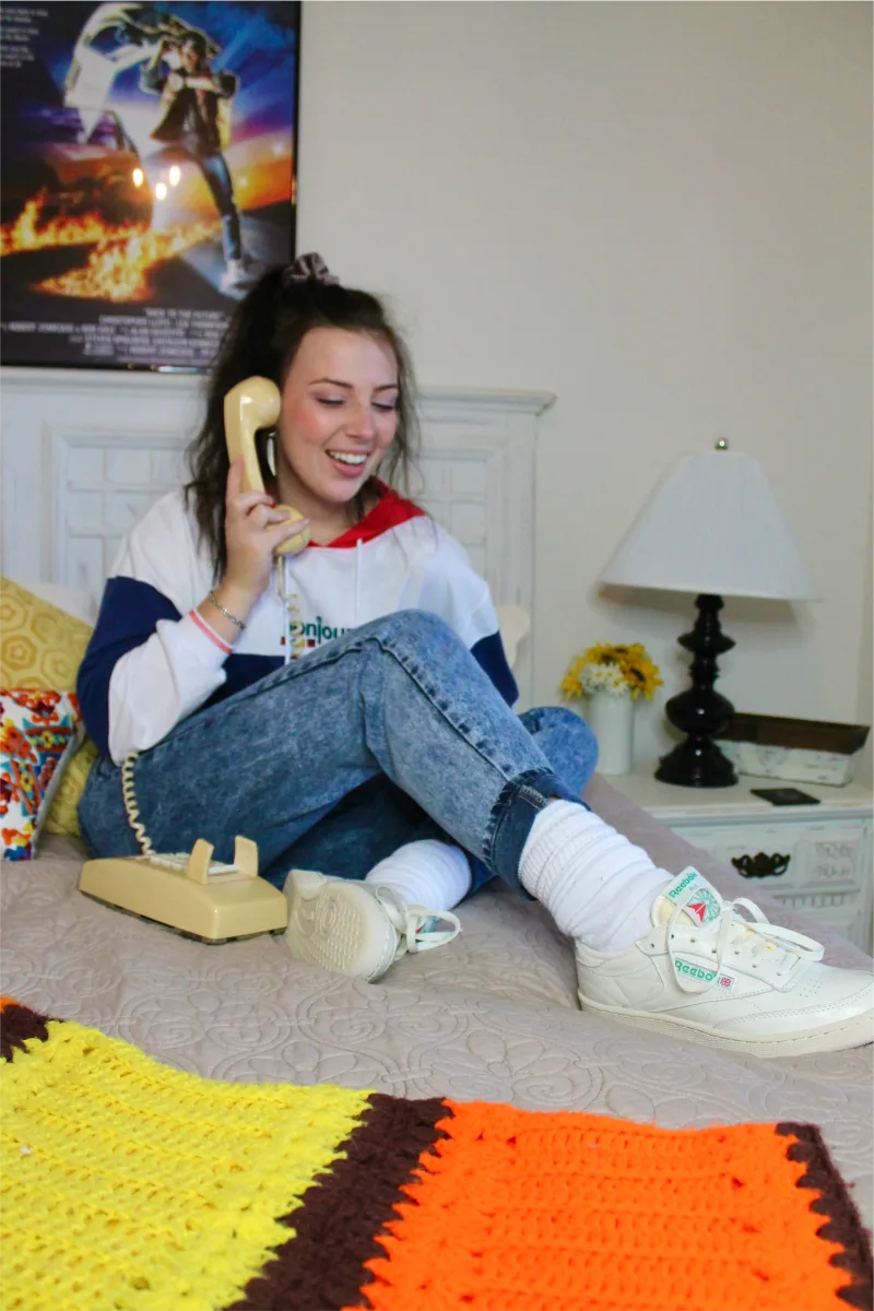 Creator in vintage clothing talks on phone on bed wearing Reebok Club C shoes