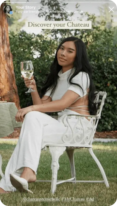Creator drinking white wine in garden stares into camera with text overlay reading Discover your Chateau
