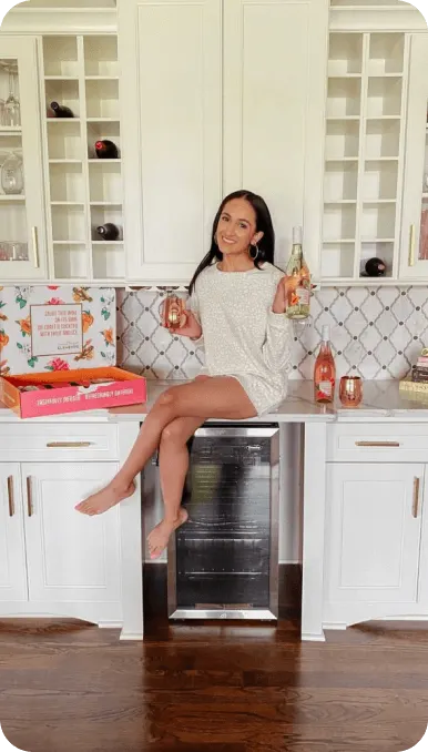 Creator poses sitting on white countertop with a glass of wine and a bottle of wine