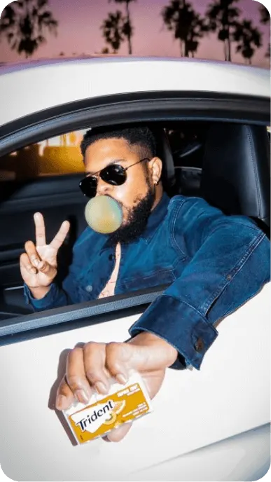 Creator chews and blows a bubble with Trident while driving white car