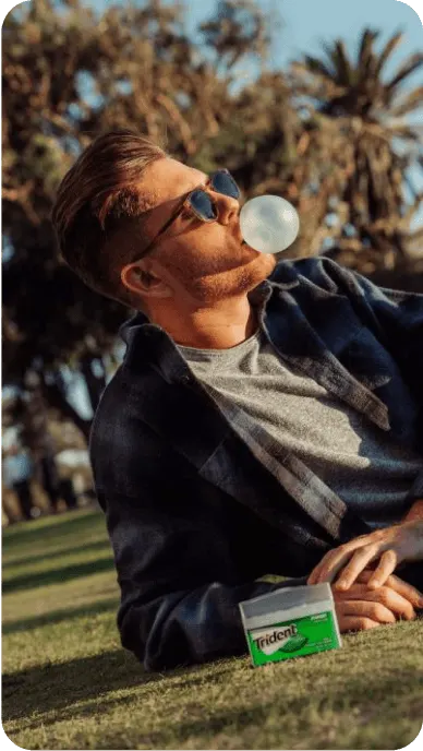 Creator blows bubble with Trident while reclining on grass